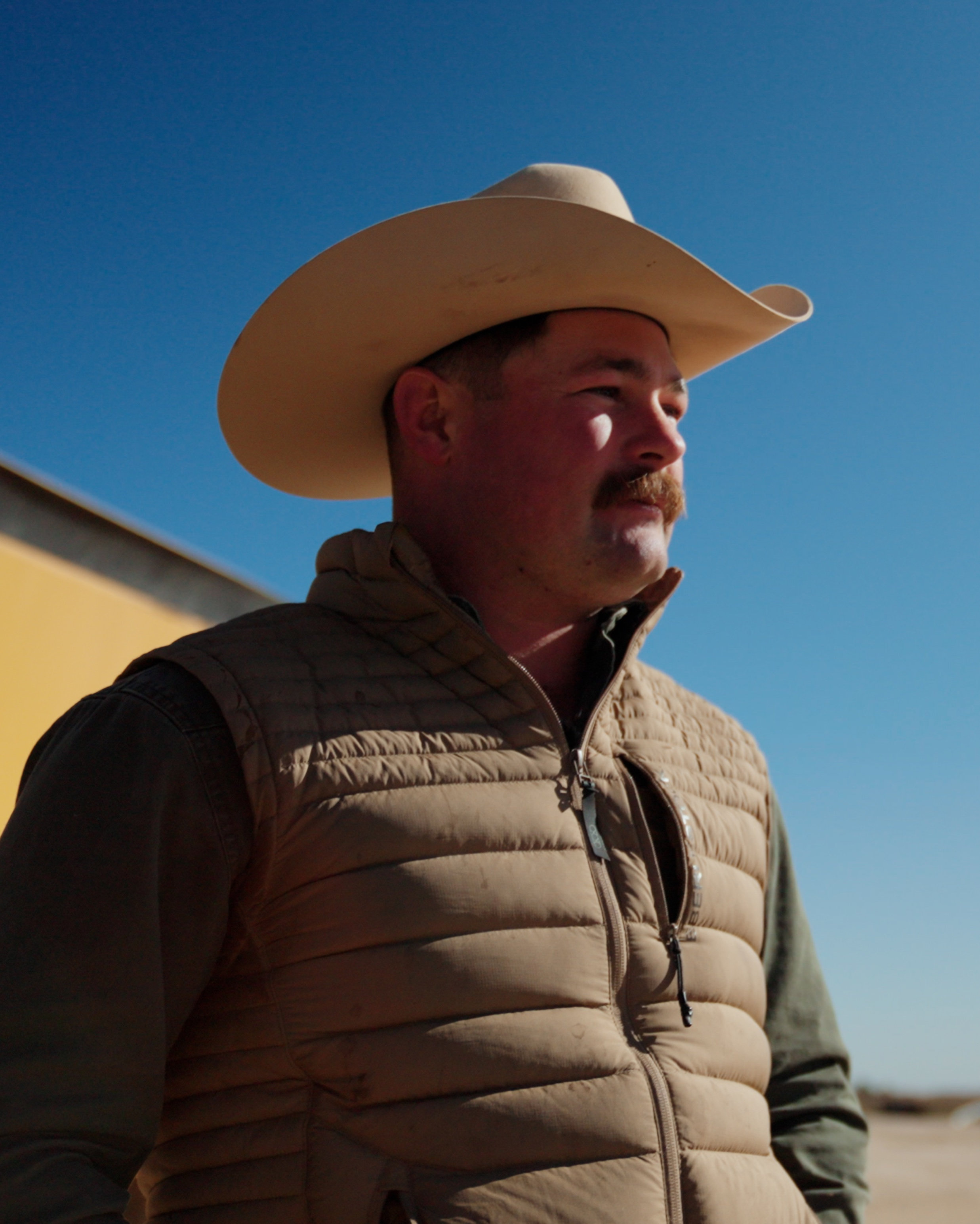 Josh McKinney, a rancher in a cowboy hat, standing in his ranch with his cattle