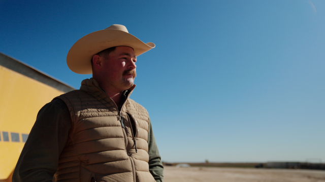Josh McKinney, a rancher in a cowboy hat, standing in his ranch with his cattle